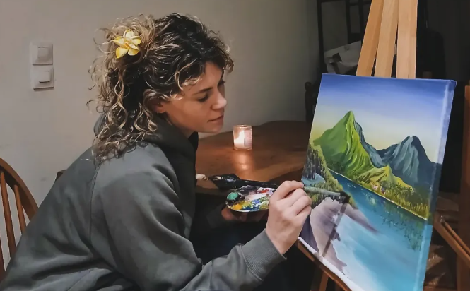 Fafa peignant un paysage de montagnes et d'océan sur une toile dans son atelier