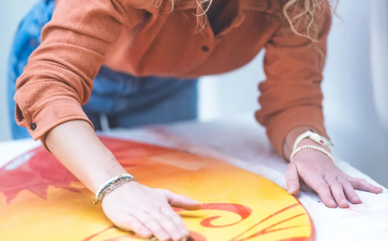 Fafa peignant à la main un motif de soleil sur une planche de surf